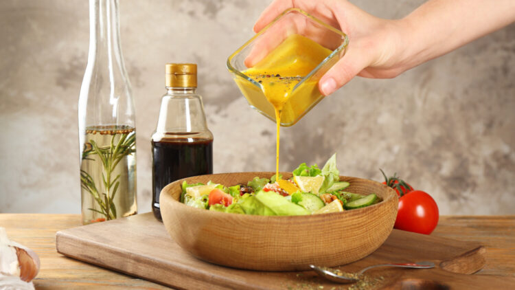 Hand pours creamy dressing on salad